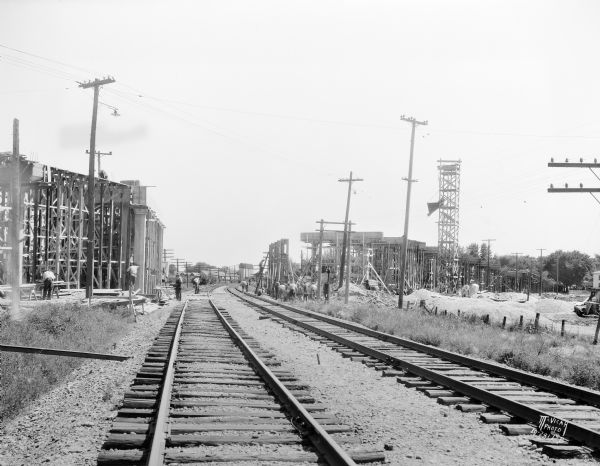 View from the west down two sets of railroad tracks towards men working on the Evansville overhead road which is under construction.