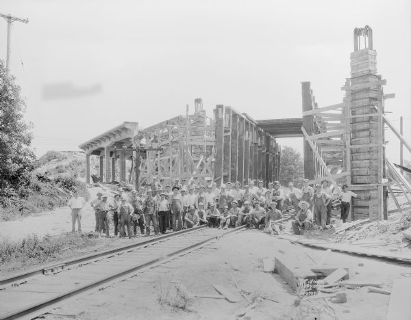 Group portrait of workmen in front of the Chicago, Milwaukee and St. Paul railroad viaduct (Olin Avenue - US Highway 12) that is under construction.
