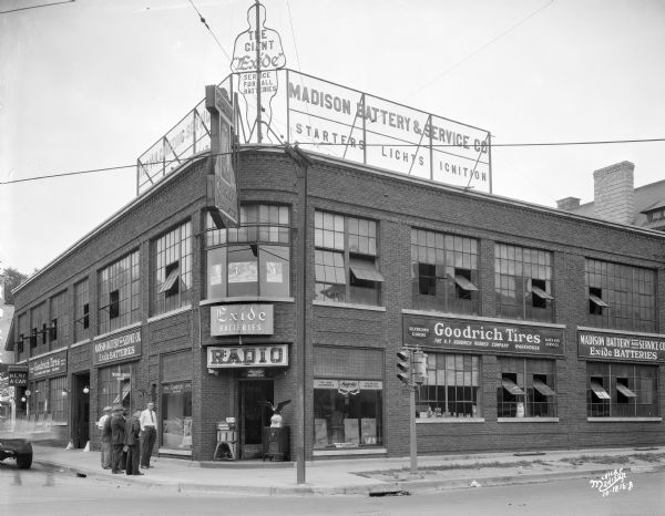 View from intersection towards the Madison Battery & Service Co. building at 250 State Street. The building is on the corner of West Johnson & North Henry Street. Advertising signs are for Exide batteries, Goodrich tires, and Majestic radios.