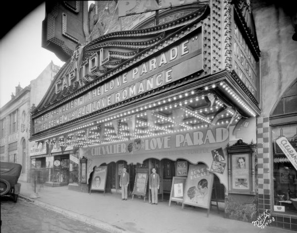 Slightly elevated view from street towards ushers posing in front of the Capitol Theatre. The marquee reads: "Maurice Chevalier in 'The Love Parade.'"