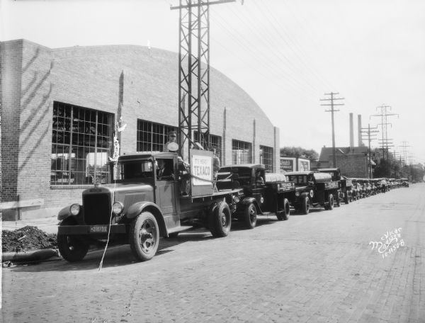 View down street towards 23 trucks and cars that were in a parade celebrating the completion of the takeover of the Capitol Oil Co. by Texaco, 919 E. Main Street, taken for Relay Motors Corp.