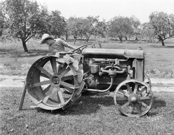 Right side view of a man sitting near an orchard, on a Fordson tractor, removing the rims.