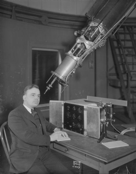 A man is sitting near a new photo electric cell equipment at Washburn Observatory on the University of Wisconsin-Madison campus. Also shown is a portion of the observatory's telescope.