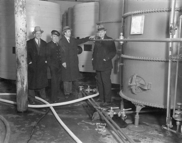 Four men are standing in the tank room at Fauerbach Brewing Co. One of the men is turning a valve. The photograph was taken to mark the modification of the Volstead Act which allowed for the legal sale of beer which began three days later.