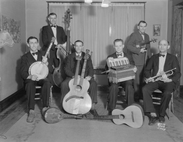 Group portrait of musicians and their instruments in Clarence Fehling's Old Timer's Orchestra, which will play for a benefit dance at East High School for the Capital Times — Family Welfare Kiddie Camp. Taken at Clarence Fehling house, 2409 Sherman Avenue.