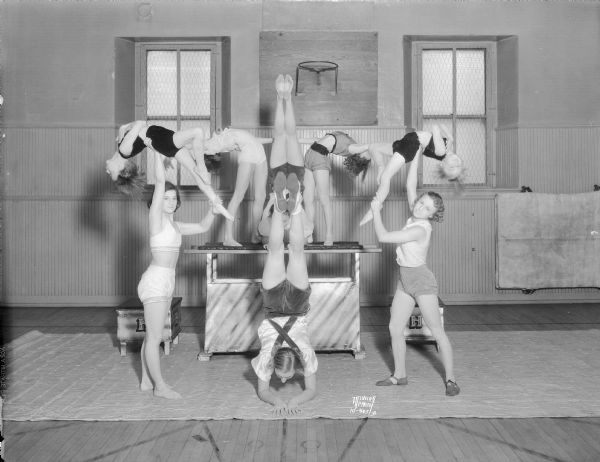 Eight girls and women, coached by J.C. Haberman, in acrobatic / gymnastic poses at the Madison Turners Hall, 21 S. Butler Street.
