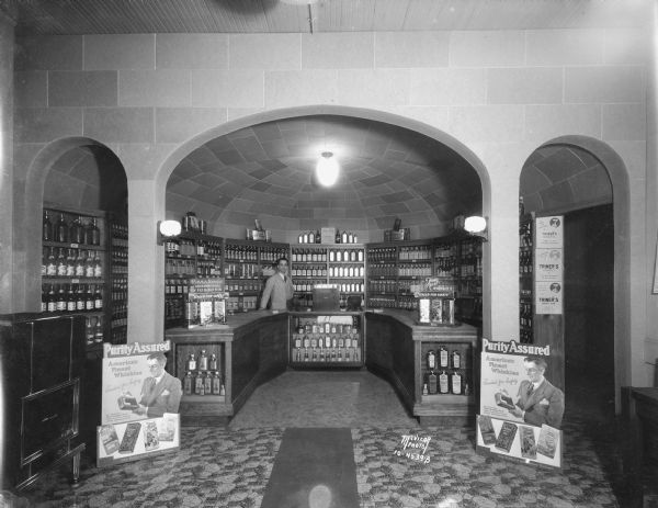 Rathskeller Inc., 122 E. Washington Avenue, liquor store interior, framed with arches, with a clerk behind the counter.