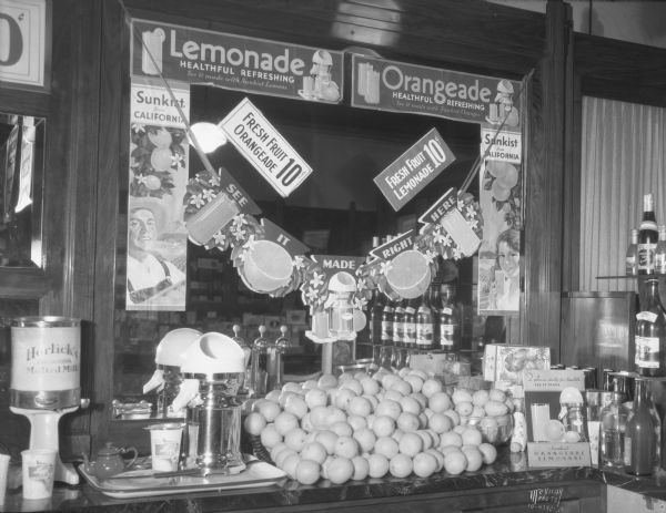 Ligget's Drug Store at 29 S. Pinckney Street, with a lemonade display on the soda fountain. The signs on the mirror read: "Lemonade healthful, refreshing," "Orangeade, healthful, refreshing." On the far left is a can of Horlick's, The Original Malted Milk, on a dispenser.