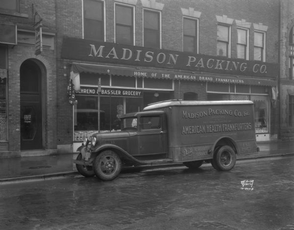 View across street towards a Ford Refrigerator truck parked along the curb outside of the Madison Packing Company at 307 W. Johnson Street. The sign painted on the side panels of the truck read: "Madison Packing Co. Inc. Originators and Sole Manufacturers of American Health Frankfurters, Americas finest frankfurter. Daily refrigerator service. Est. 1913."