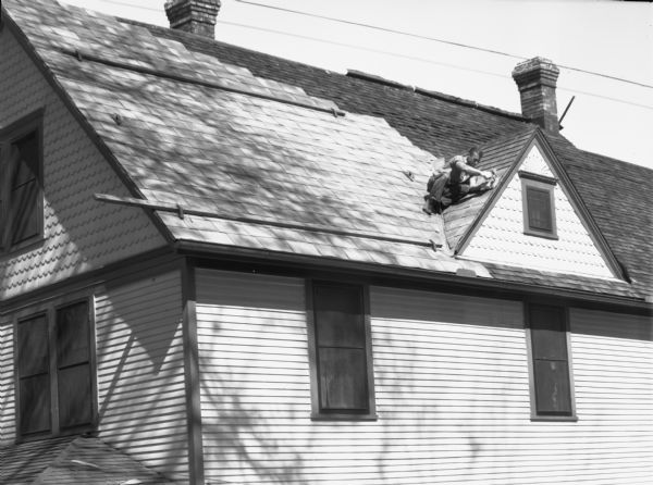 View looking up towards a man laying new shingles on the roof of a house at 341 West Wilson Street.