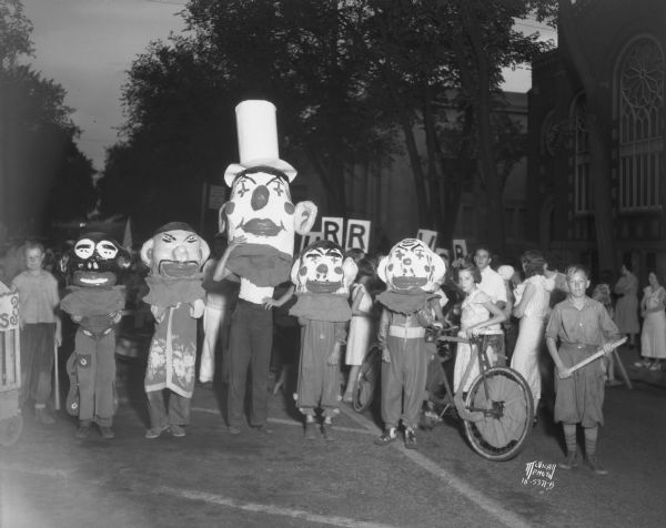 Children, from Hawthorne School Annex, wearing Mardi Gras style heads, are marching in the Lantern Parade, with the First Evangelical Church in the background, on 221 Wisconsin Avenue.