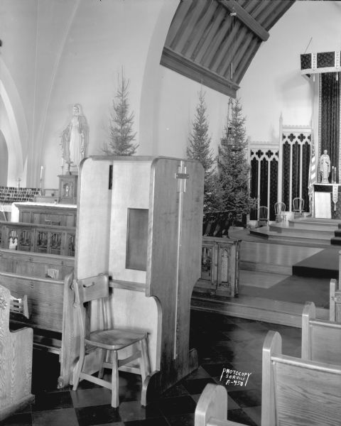 Portable confessional set up at Blessed Sacrament Catholic Church, 2119 Rowley Avenue. This view shows the priest's side with a 
chair. Photograph was taken for Burgess Laboratories.