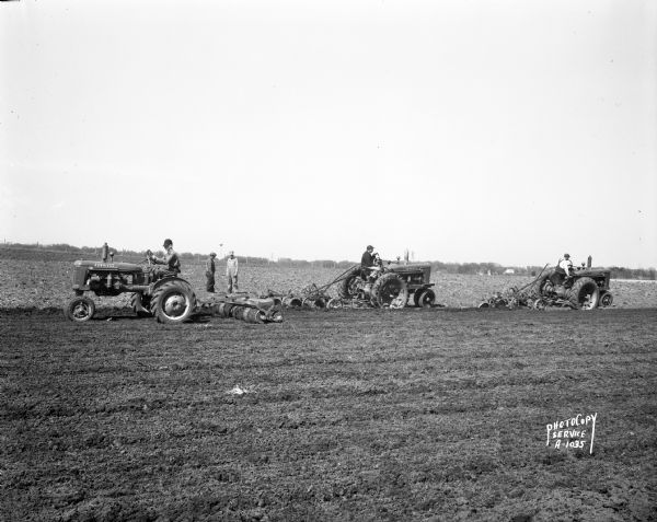 View of Wisconsin Conference of Seventh Day Adventists farm field, with two farmers watching three other farmers on Farmall tractors. They are plowing and discing a field on Duborg Road off of Highway 16 west of Columbus.