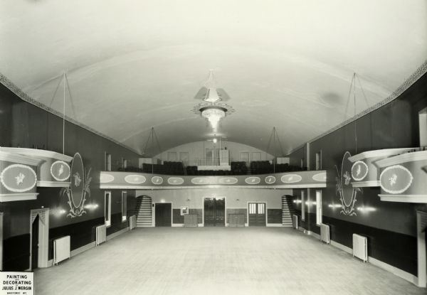 Elevated view of the rear of the New Opera House at 411 N. 8th Street following remodeling, with its ornately decorated walls, tiered boxes and projecting balcony. A large crystal chandelier, bracketed wall lighting and reflective, light-colored ceiling provide illumination. Open doorways, normally velvet draped, lead to upper-level seating. Steam-heat radiators line the walls. Painting and decorating by Julius J. Wergin.  