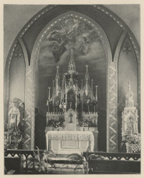 Gothic arches frame the intricately designed and decorated altar of the Sacred Heart chapel. Across the front of the high altar, from left to right, are statues of St. Anthony of Padua, a Franciscan Saint who is very special to the Franciscan Order, the Blessed Virgin Mary with a crown of stars around her head, a statue of the Sacred Heart of Jesus, St. Joseph holding the child Jesus, and on the right is St. Francis holding a crucifix. The larger statue to the left of the altar is Mary holding the Infant Jesus, and on the right is the Infant of Prague. Eleven angels in the painting above hold a banner reading "Venite adoremus"; Come let us adore. Three Latin words above the angels are, possibly: "Sanctus, Sanctus, Sanctus"; Holy, Holy, Holy. The descending curling banner starting on the left side reads, in English: "Come to me all you who are burdened," and continues on the right with "and I will refresh you." In the foreground are front pews, potted ferns and an open communion rail. The chapel's location was on the second floor, above the parlor, on the west side of the building and was for the use of hospital patrons and employees.<p>Description provided by the Sisters of Holy Family Convent, Franciscan Sisters of Christian Charity, O.S.F.</p>