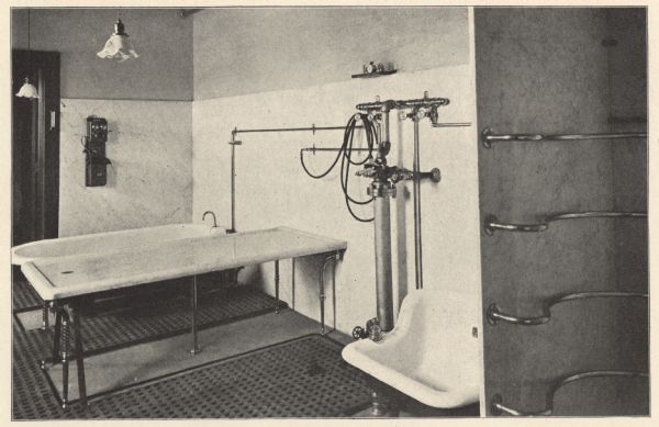 View of one of the Water Cure Department's rooms furnished with a large porcelain bath tub, marble table and sitz or hip bath. An apparatus for water regulation is mounted on the marble-lined wall with a shelf, above, holding hose nozzles and a timer or small clock. A telephone is mounted on the wall next to a wooden door frame. On the right is a marble wall partition with four curved bars dividing what is probably the site of vertical and horizontal showers from the rest of the room. Areas of the cement floor have a drainable covering, possibly made of rubber.  The following is quoted from the hospital's 1902 patient booklet: "The Hydrotherapeutic (Water Cure) Department is a feature to which we desire to call special attention. It is located in the basement, and is equipped with all the modern appliances, affording ample facilities for the application of the various forms of Hydrotherapy. Hot baths, steam cabinets, and Turkish baths are provided with the very best modern equipment. Trained and experienced attendants are in charge for both men and women. Massage treatments are administered according to the famous German method." 