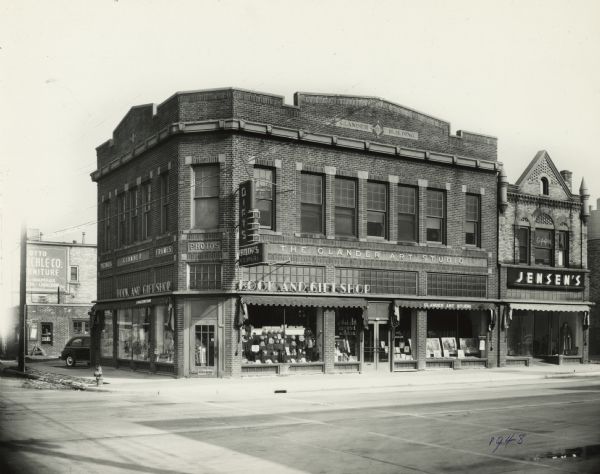 View across street towards the Glander Building, built by photographer John A. Glander, on the northeast corner of S. 9th and Washington Streets. The Glander Art Studio, 822 Washington Street, occupies the second floor and right side of the ground and lower level. The Book and Gift Shop, 824 Washington Street, occupies the left side. The adjoining building, also owned by Glander, is occupied by Jensen's. The word "GLANDER" appears as a graphic design in the second floor window.  Studio workrooms were on the 2nd floor of this building. This image appears in the <i>Manitowoc Herald-Times'</i> Washington Street paving edition of Nov. 3, 1948. Concrete paving has replaced the old brick and asphalt street. The photograph's caption states that the Glander Art Studio is celebrating its 40th anniversary. Services  and items offered are  portrait and commercial photography, picture framing, frames, pictures for decoration, Eastman Kodaks, Kodak finishing and Spode dinnerware. Glander's gift shop, which had originally occupied the entire 1st floor, was discontinued in 1936. The floor was divided and rental space made available. The Book and Gift Shop, owned by Violet and Norbert Kustka, carries books, school and office supplies, greeting cards, gifts, religious supplies and toys, which are on the lower level. Their shop was in this location from 1943-1955, when it moved to 831 S. 8th Street. The Jensen Ready-To-Wear Shop at 820 Washington Street, owned by Clarence Jensen and managed by Laura Beaton, features women's and children's clothing. Jensen's occupied this location, which was a branch of their main Two Rivers store, from 1938-1950. The Two Rivers store continued in operation.