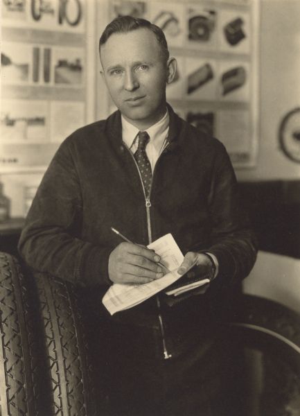 Standing, three-quarter length portrait of Edward J. Carlier (1893-1954) posing with an elbow resting on tires and a pencil and papers in his hands. Established in 1926 at 708 York Street, Carlier Tire Service relocated the following year to larger facilities at 718-720 Commercial Street (now Maritime Drive). The company offered new and used tires, tire repairing and 24-hour road service, which was an uncommon practice at the time. Battery sales and service were added in 1932. Newspaper advertisements stated they repaired rubber bathing suits, as well. Mr. Carlier creatively promoted his business. He drove a car up the courthouse steps to demonstrate the durability of ballon tires, which were introduced in the 1920s. During inclement weather, he drove around the county and reported road conditions back to a local radio station. In 1936 he sold the business to his brother-in-law, Ray L. Timm. Carlier also had an appliance business. His inventive nature led him to create and manufacture gas and electric appliances, including a gas toaster, and to other business pursuits.  He was a sergeant in the Army Air Service in World War I, working as an aircraft mechanic at Rockwell Field in California. He was a charter member of both the Last Man's Club, made up of WWI veterans, in 1927 and Forty et Eight, Manitowoc County Voiture (boxcar), No. 1130, in 1934.  In 1933 he was named commander of the American Legion, Guy Drews Post.