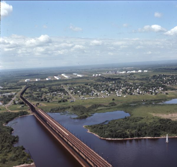 Aerial view of an ore dock next to Hog Island. The town is in the distance. In the far background are the white storage buildings of the oil refinery.