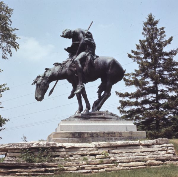 A bronze statue of an American Indian man riding a horse. Words carved into the base of the stone pedestal read: "The gift of Clarence Addison Shaler."