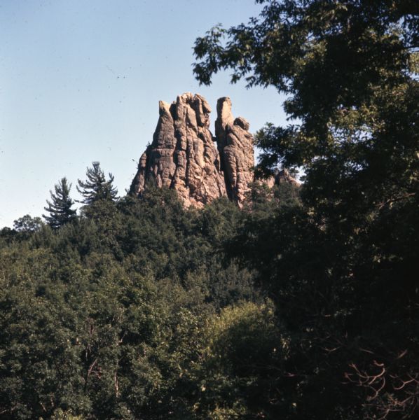 View through trees towards a rock outcropping rises above the tree line.