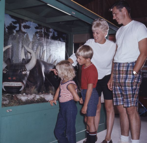 A family looking at a sculpture of a Hodag in a glass case at the Rhinelander Logging Museum.