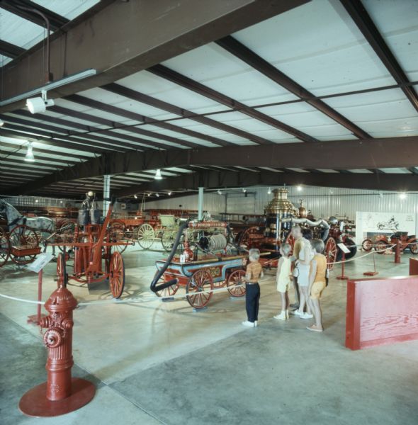 A family looking at an exhibit at the Hall of Flame Fire Museum. The exhibit contains motorized and horse-drawn fire engines, as well as fire pumps. 