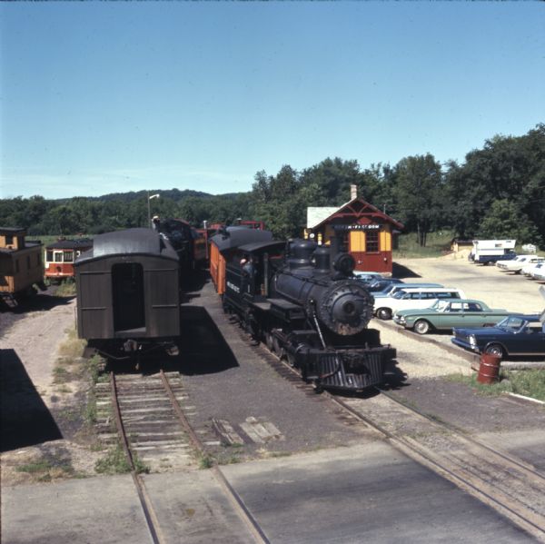 Elevated view of steam trains and railroad cars on the North Freedom Railroad at the Mid-Continent Railway Museum. Cars are in the parking lot on the right near the station.