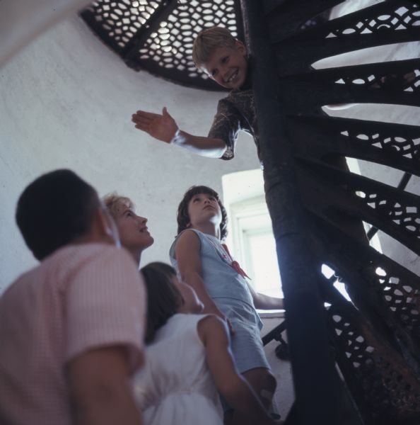 A family of five is climbing up the spiral stairs of the Eagle Bluff Lighthouse. The young boy in the lead is leaning down and offering a high five.