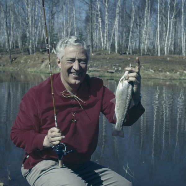 Governor Warren Perley Knowles, 37th Governor of Wisconsin, holding up a rainbow trout at Teal Lake. He is holding his fishing pole in his right hand, and the trout in his left hand.