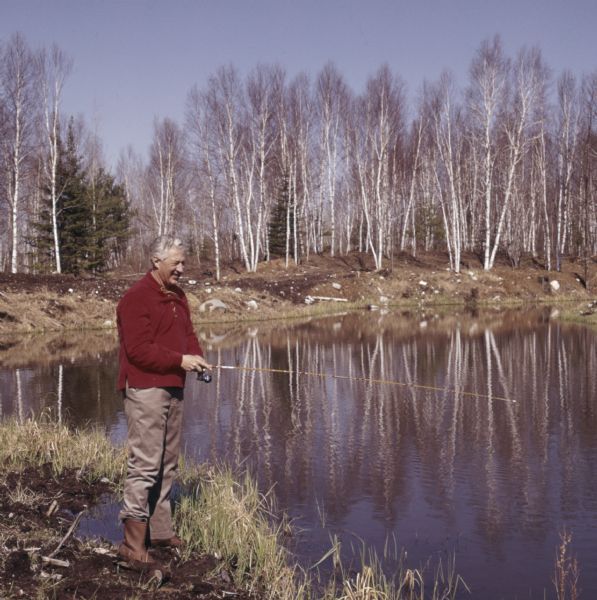 Governor Warren Perley Knowles, 37th Governor of Wisconsin, standing on the shoreline of Teal Lake holding a fishing pole.