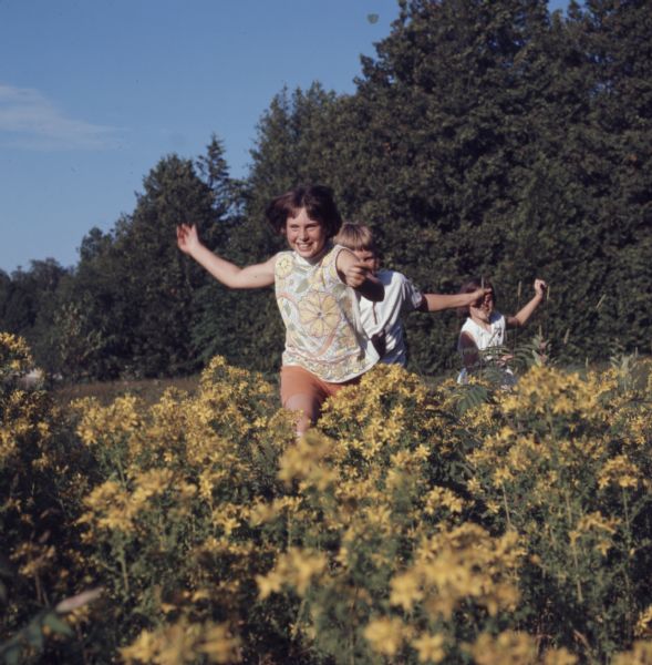 Three children are running through a field of yellow flowers.