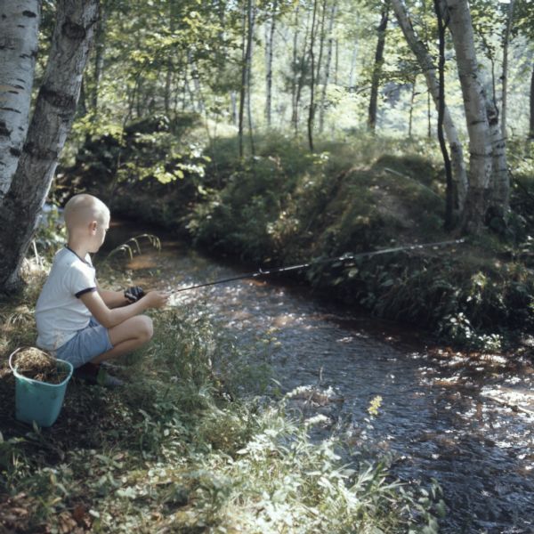 A young boy is sitting on a riverbank fishing along the banks of the Crystal River. 