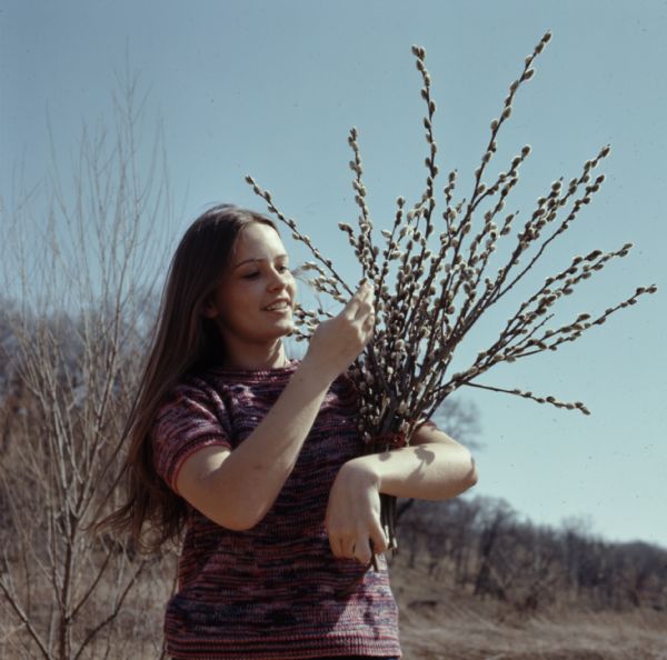 Jackie Thompson standing outdoors holding a bundle of pussy willow branches.