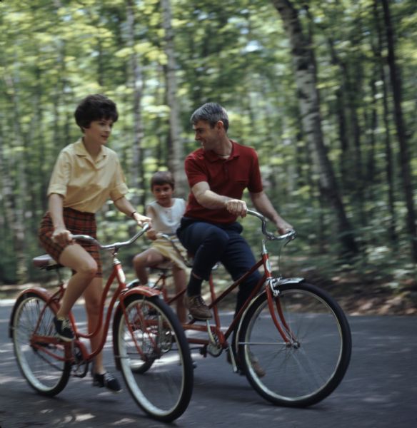 A family of three is biking down a paved road in Peninsula State Park. The child is riding a tandem bike with the father.