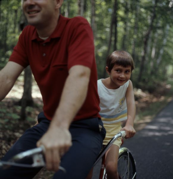 Close-up view of a father riding a tandem bike with his child.