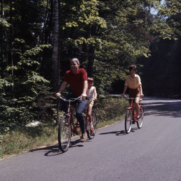 A family of three is biking down a paved road in Peninsula State Park. The child is riding a tandem bike with her father.