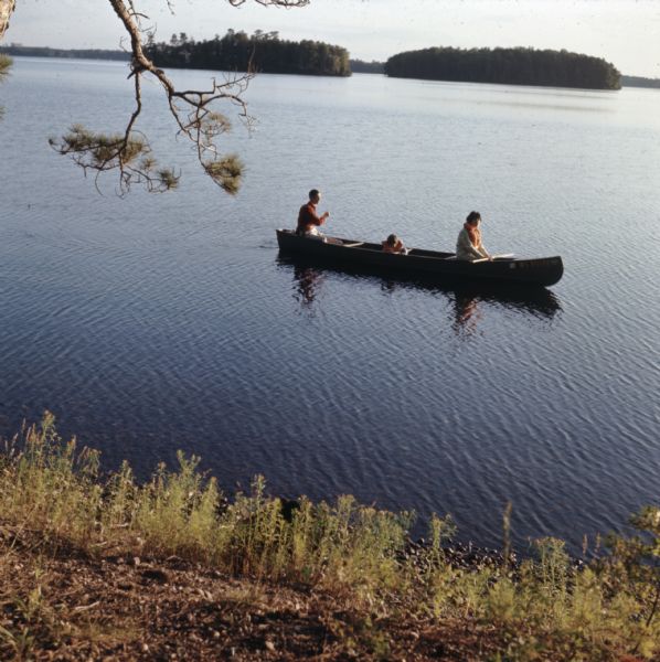 View from shoreline of three people canoeing on Trout Lake.