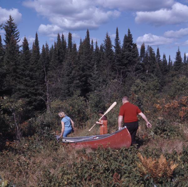 A family of three are portaging their canoe through the brush and trees on the Brule Portage Trail.