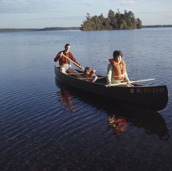 View across water towards a family of three canoeing on Trout Lake.