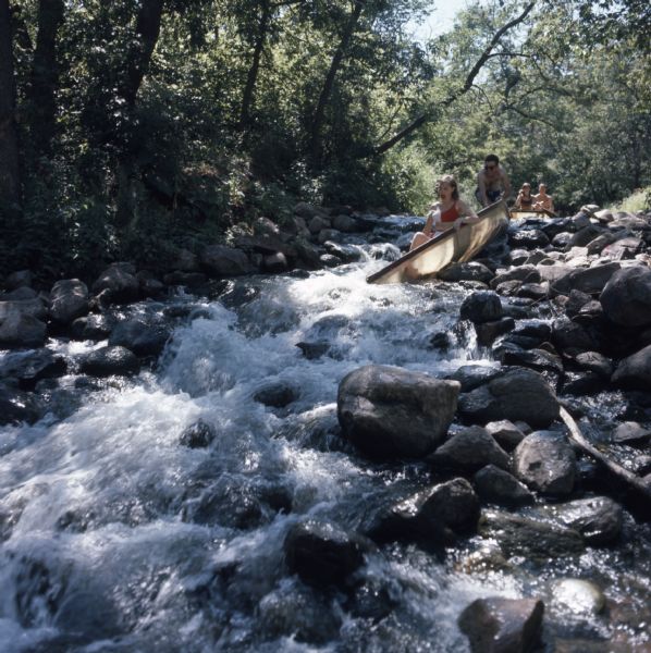 A young woman is sitting in a canoe at the top of white water rapids on the Crystal River. A young man is holding onto her canoe. Behind them a man and woman are sitting in a canoe waiting their turn.
