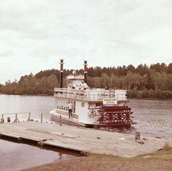 Men, women, and children are on a riverboat named "Namekagon Queen," which is on the Namekagon River next to a wooden dock.