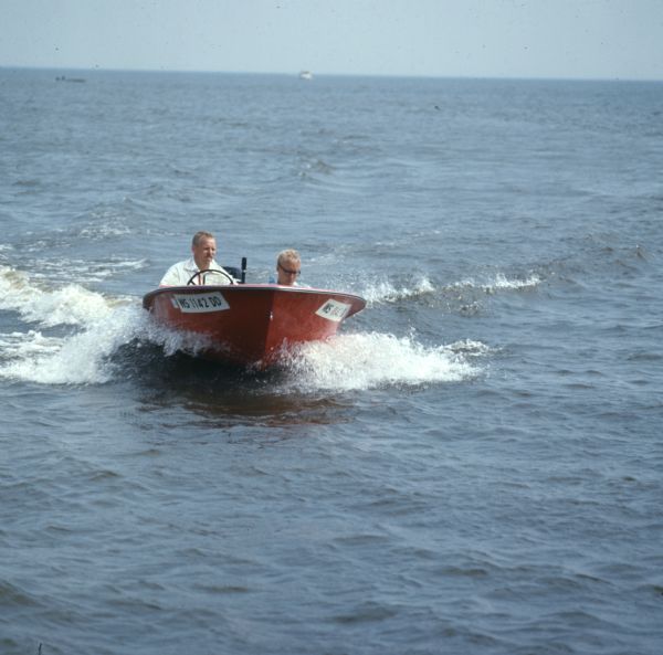 View towards two men riding in a red motorboat on a lake.