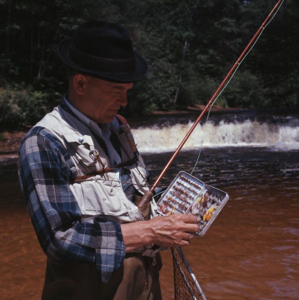 Close-up of a man examining the contents of his fly-fishing tackle box while standing in Robinson Creek.