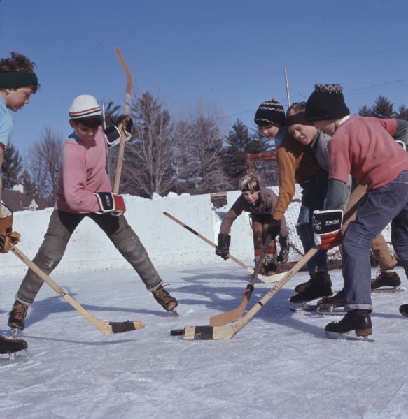A group of children playing hockey on an outdoor ice rink.