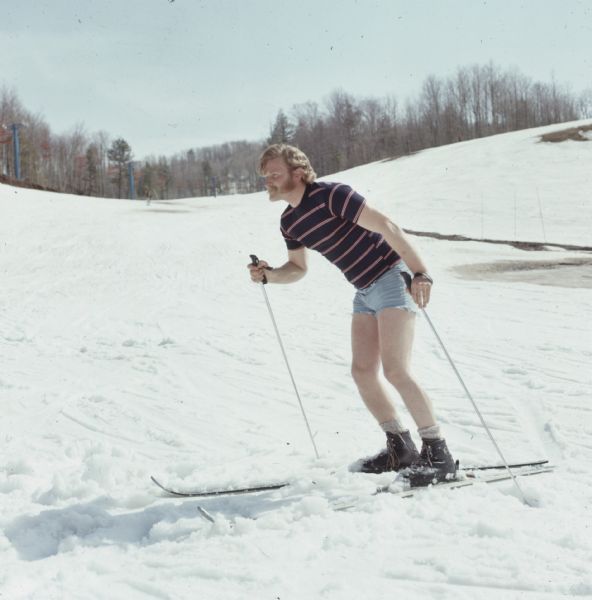 A man is skiing down a hill wearing a striped t-shirt and shorts.