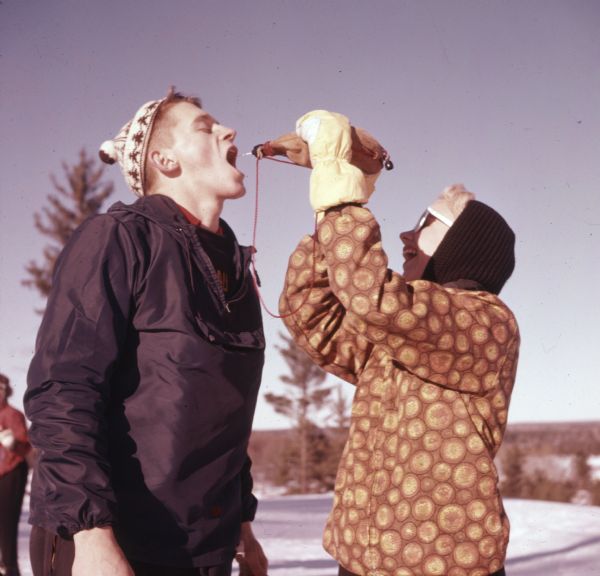 A woman is squirting water from a canteen into a man's mouth at Mt. Telemark Resort.