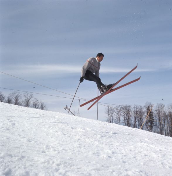 A man wearing skis is jumping off the snow-covered ground and supporting his weight on ski poles.
