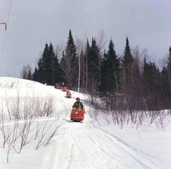 View looking towards a group of people driving snowmobiles down a hill.