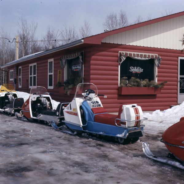 A line of snowmobiles parked in front of a restaurant.